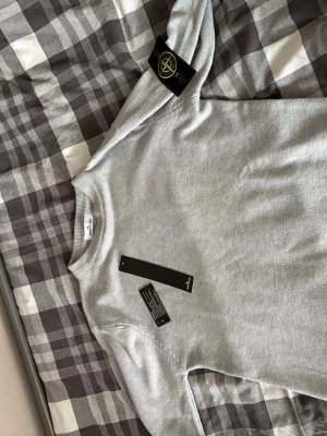 Ljusgrå  Stone Island tröja  - Snygg ljusgrå tröja från Stone Island med klassisk rund halsringning. Tröjan har den ikoniska Stone Island-loggan på vänster ärm och är tillverkad i mjukt material som passar perfekt till vardagslooken.
