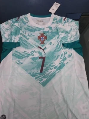 Portugal fotbollströja mintgrön - Snygg Portugal fotbollströja i mintgrönt och vitt med nummer 7 på framsidan. Tröjan har ett mönstrat tryck, rund halsringning och korta ärmar. Perfekt för fotbollsträning eller att bära som supporter.