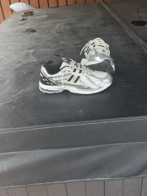 Silvriga och vita sneakers - Snygga sneakers i silver och vitt med svarta detaljer och vita skosnören. Skorna har en sportig design med mesh och syntetmaterial, samt en bekväm sula som passar perfekt till streetwear eller casual outfits.
