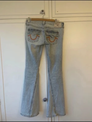 Ljusblå bootcut jeans från true religion  - Säljer ett par ljusblå bootcut jeans från true religion med snygga broderade detaljer på bakfickorna. Jeansen har klassisk femficksmodell och utsvängda ben. Perfekta för dig som gillar retrovibbar och vill sticka ut lite extra.