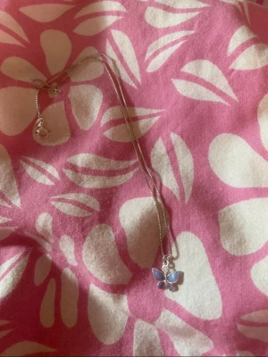 Silverhalsband med blå fjärilshänge(barn) - Sött halsband i silverfärg med ett hänge format som en fjäril. Fjärilen har blå och lila detaljer som skimrar fint. Kedjan är tunn och smidig, perfekt för att ge en extra touch till din outfit.