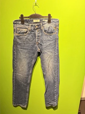 Blå raka jeans med kontrastsömmar - Säljer ett par klassiska blå jeans med raka ben och kontrastsömmar. Jeansen har fem fickor, normal midja och snygga slitningar framtill. Materialet är kraftig denim och bakfickorna har dekorativa sömmar. Perfekta för en avslappnad och trendig look.