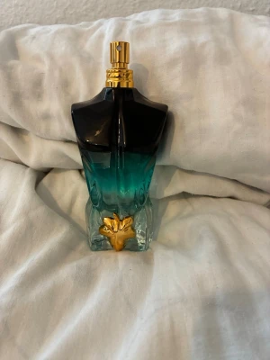 Jean Paul  - Le beau parfum 125 ml helt ny.Snygg parfymflaska i form av en manlig torso med blå-grön färgton som övergår till svart upptill. Flaskan har en guldfärgad spraydel och en dekorativ guldfärgad detalj framtill. Perfekt som både doft och inredningsdetalj. Helt ny och säljer denna eftersom att jag beställde fel.
