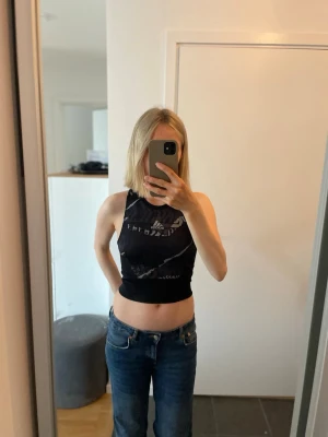 Svart croppad träningstopp från Adidas - Säljer en svart croppad linnetopp från Adidas i storlek S med grått litet tryck. Toppen har en tight passform med hög rundad hals. 20 kr!