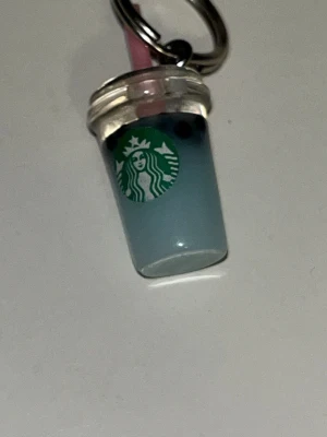 Starbucks nyckelring med blå dryck - Söt nyckelring formad som en Starbucks-mugg med blå dryck och sugrör. Muggen har det klassiska gröna Starbucks-logotypen på framsidan och är gjord i plast. Perfekt accessoar till väskan eller nyckelknippan för dig som älskar kaffe och coola detaljer.