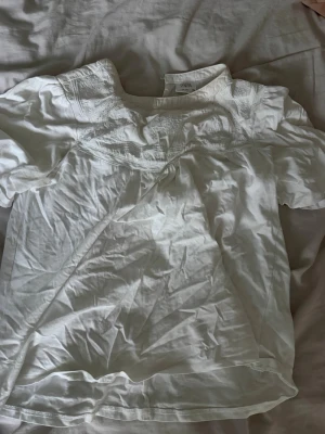 Vit blus med broderi från Zara - Säljer en vit blus från Zara med fina broderade detaljer upptill. Blusen har korta ärmar och en lös, luftig passform. Perfekt till jeans eller kjol för en fräsch och enkel look. liten sminkfläck men går säkert bort i tvätten annars inget man märker.