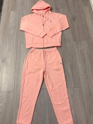 Rosa mjukisbyxor från Polo Ralph Lauren - Säljer ett par ljusrosa mjukisbyxor från Polo Ralph Lauren med blå logga broderad på benet. Byxorna har resår i midjan och är gjorda i mjukt bomullsmaterial. Perfekta för chill dagar eller när du vill vara extra bekväm.