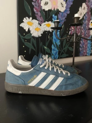 Adidas blå Spezial sneakers - Säljer ett par Adidas Spezial sneakers i blå mocka med vita detaljer och klassiska tre ränder på sidan. Skorna har vita snören, grå sula och gul Spezial-logga. Perfekta för dig som gillar retrostil och streetwear.