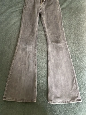 Svarta utsvängda jeans - Säljer ett par svarta jeans med utsvängda ben och hög midja. Jeansen har klassisk femficksdesign och dragkedja fram. Perfekta för dig som gillar retrostil och vill ha ett par riktigt snygga jeans med 70-talsvibbar. Svarta med gråa toner. På bilderna ser dom ljus gråa ut med dom är svarta.