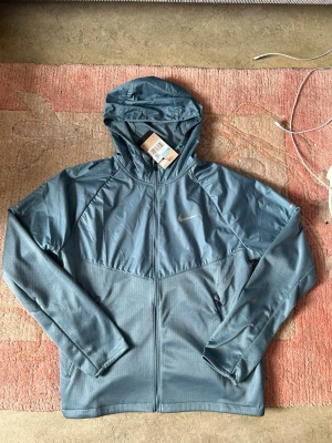 Nike jacka  - Säljer denna riktigt snygga Nike running jacket i storlek M, helt ny med tags och kvitto kvar, jackan är riktigt bekväm och är även justerbar i storleken, perfekt för idrottsaktiviteter etc, köpt i Estland, pris kan diskuteras!! Tveka inte att skriva!!