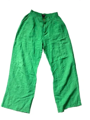 Gröna vida linnebyxor - Snygga gröna linnebyxor med hög midja och vida ben. Byxorna har knapp och dragkedja framtill samt fickor i sidorna. Perfekta för en avslappnad och trendig look under varma dagar.