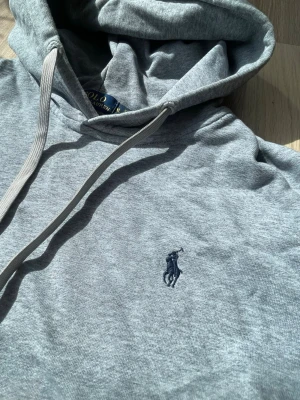 Grå hoodie från Polo Ralph Lauren - Säljer en stilren grå hoodie från Polo Ralph Lauren med klassisk huva och dragsko. Storleken är slim fitt xl vilket är ungefär M. (Passar runt 170-180 cm, 65-75 kg)
