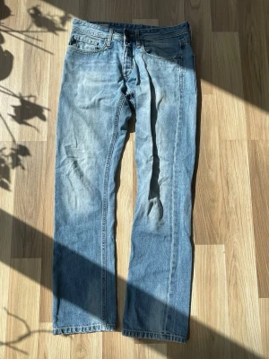 Ljusblå raka jeans från jacka and jonses - Säljer ett par ljusblå jeans från jack and jones med rak passform och slitna detaljer vid benslut. Jeansen har klassisk femficksmodell, dragkedjegylf och är tillverkade i denim. Perfekta för en avslappnad och trendig look. Mfg originals
