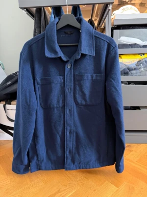 Mörkblå overshirt från D'once De La Sense - Snygg mörkblå overshirt med två stora bröstfickor och knäppning framtill. Skjortan har klassisk krage och långa ärmar. Perfekt lager på lager-plagg för en avslappnad stil.