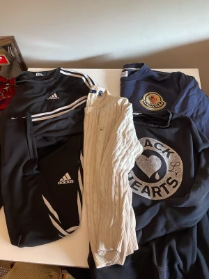 Svart Adidas tröja med vita ränder - Svart långärmad tröja från Adidas med klassiska vita ränder längs ärmarna och adidas -logga på bröstet. Sportig och avslappnad stil, perfekt till jeans eller träningsbyxor.