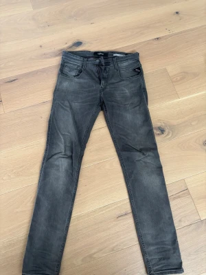 Mörkgrå slim jeans från replay - Snygga mörkgrå jeans i slim fit med klassisk femficksdesign och dragkedja. Jeansen har diskreta slitningar och raka ben, perfekta till en avslappnad stil. Materialet känns mjukt och följsamt, troligen bomull med lite stretch. 28/30 storlek 