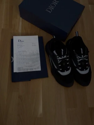 Svarta Dior B22 - Säljer ett par snygga Dior sneakers i svart och vitt med coola detaljer och klassisk snörning. Skorna har en sportig siluett och är tillverkade i en mix av läder och textil. Kommer med originalkartong och dustbag.