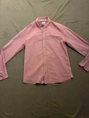 Rosa långärmad skjorta i bomull - Snygg rosa skjorta med klassisk krage och bröstficka. Skjortan är långärmad och har knappar framtill. Tillverkad i mjuk bomull, perfekt för en avslappnad men stilren look.