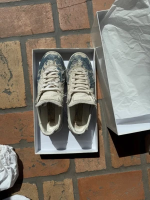 Vita och blå Maison Margiela  - Unika sneakers i vitt med blå färgstänk och slitna detaljer. Pris går att diskutera 