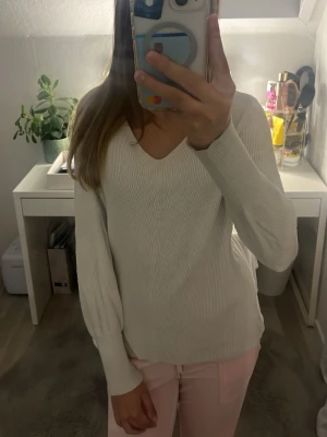 Off-white stickad tröja från ONLY - Säljer en stilren off-white stickad tröja från ONLY med v-ringning och långa ärmar. Tröjan har en ribbad struktur och är perfekt för lager på lager. Enkel att matcha med olika outfits och superbekväm att bära.