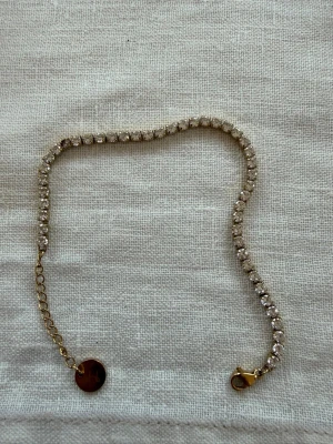Guldarmband med glittrande pärlor - Snyggt armband i guldton med glittrande, klara pärlor längs hela bandet. Armbandet har en tunn kedja och ett runt hänge vid låset. Perfekt för dig som gillar stilrena och eleganta accessoarer.