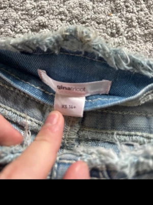Ljusa jeans från Gina Tricot - Säljer ett par ljusblå jeans från Gina Tricot i storlek XS. jeansen har råa, fransiga kanter upptill, klassiska fickor fram och bak samt bälteshällor.