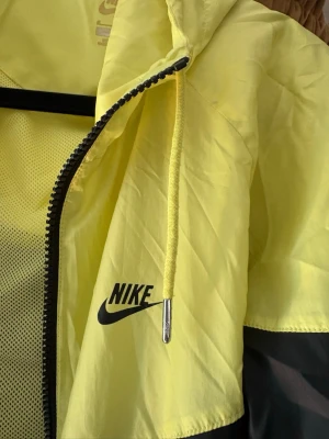 Gul och svart vindjacka från Nike - Snygg vind/träningsjacka från Nike i gul och svart med dragkedja framtill och huva med snörning. Perfekt för en sportig look till träningspasset 💫