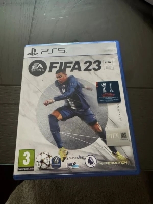 FIFA 23 till PS5 - FIFA 23 till PlayStation 5 med blå plastfodral. Omslaget visar en fotbollsspelare i action och spelet har officiella logotyper för bland annat Premier League och UEFA Champions League. Perfekt för dig som gillar fotbollsspel och vill spela med de största lagen.