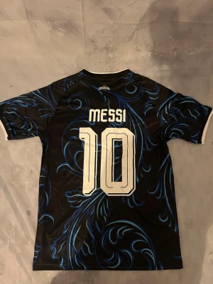 Argentina Messi matchtröja svart/blå - Säljer en svart och blå Argentina matchtröja från Adidas med Messi och nummer 10 på ryggen. Tröjan har vita detaljer, FIFA-märke och AFA-logga på bröstet samt snyggt mönster i blått. Perfekt för dig som älskar fotboll och vill sticka ut på planen.