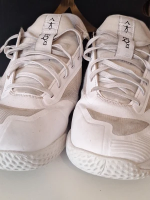 Vita kanso innebandy skor - Snygga vita sneakers med svart detalj på sidan och meshpaneler för extra ventilation. Skorna har vita snören och en tjock, strukturerad sula som ger bra grepp. Perfekta för dig som gillar en clean och sportig look.
