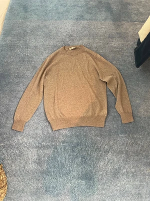 Beige stickad tröja från Canali oanvänd utan prislappar - Snygg beige stickad tröja från Canali, tillverkad i Italien. Tröjan har rund halsringning, långa ärmar och ribbade muddar vid ärmslut och nederkant. Perfekt för dig som gillar klassisk och stilren design från italien. Tröjan är super lätt i ett matrial från canali som heter traveler merino wool och är mjukare än en standard cashmiere