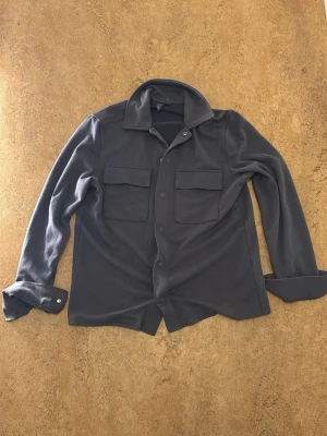 Grå overshirt - Snygg grå overshirt med en ficka på varsitt bröst, använd några gånger men har fof ingen syn på använding eller har några defekter
