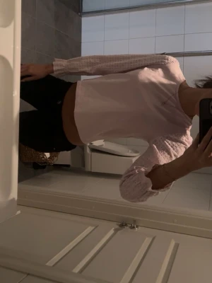 Ljusrosa blus med volangärmar - Söt ljusrosa blus med långa, lätt transparenta ärmar och volangdetaljer vid ärmslut. Blusen är croppad och har en enkel, stilren design som passar perfekt till jeans eller kjol.