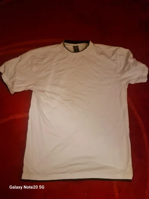Vit t-shirt från Urban Classics XXL - Klassisk vit t-shirt från Urban Classics i storlek XXL. T-shirten har rund hals med svart kant och är tillverkad i mjuk bomull. Enkel och stilren design som passar till det mesta. Perfekt basplagg för garderoben.