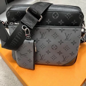 Monogram crossbody väska - Snygg crossbody handväska i tvåtonad grå och svart färg med klassiskt monogrammönster. Väskan har bred axelrem och matchande liten accessoar. Tillverkad i slittåligt läder med silverfärgade metalldetaljer.