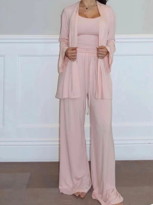 Ljusrosa loungewear-set med vida byxor - Mysigt loungewear-set i ljusrosa med matchande topp, vida byxor med resår i midjan och en öppen cardigan. Setet har en avslappnad passform och är tillverkat i ett mjukt, stretchigt material som känns skönt mot huden. Perfekt för chill dagar hemma.  Endast provad 