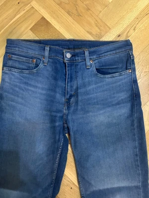 Blå Levi's 511 slim jeans - Snygga blå Levi's 511 slim jeans i klassisk femficksmodell. Jeansen har en mellanblå tvätt med subtila slitningar och är tillverkade i bomull. Passformen är smal och midjan normal. Perfekta för en avslappnad och trendig look.