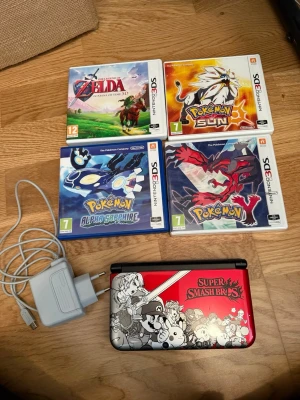 Nintendo 3DS XL Super Smash Bros Edition - Nintendo 3DS XL med röd och svart Super Smash Bros-design. Konsolen har en cool grafik med flera kända karaktärer på locket. Medföljer laddare. Perfekt för dig som gillar bärbart spelande och snygg design.