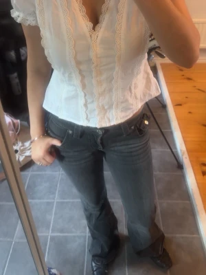 Mörk gråa true religion jeans - Säljer ett par mörkgrå bootcut jeans med låg midja och klassiska fem fickor. Jeansen har en lätt tvättad look och sitter snyggt över höfterna. Perfekta för dig som gillar en avslappnad men trendig stil. Har slitage längst ner på ena benet