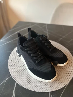 H skor sneakers  - Snygga svarta H sneakers med vit, räfflad sula och vita skosnören. Skorna har detaljer i mocka och läder, Perfekta för dig som vill ha något exklusivt och trendigt i garderoben.