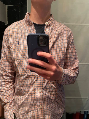 Ruting skjorta polo Ralph lauren - Säljer en klassisk rutig skjorta i orange, blått och vitt med knappar framtill och button-down krage. Skjortan har lång ärm och en liten broderad logga på bröstet. Perfekt för dig som gillar en avslappnad men ändå stilren look. Modellen är 178cm och väger 65kg. Storleken är mindre än vad som står passar s/m