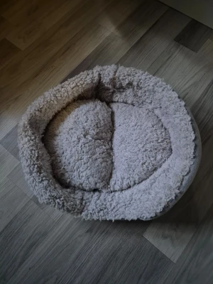 Rund fluffig djurbädd från Pet Club - Mysig rund djurbädd i ljusgrått från Pet Club. Bädden är tillverkad i mjukt, fluffigt tyg och har en upphöjd kant som ger extra komfort. Perfekt för både katter och små hundar som gillar att kura ihop sig. Mått ca 30×40 cm
