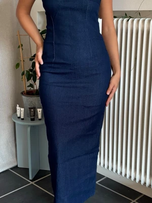 Mörkblå lång jeansklänning - En helt oanvänd, snygg, mörkblå långklänning i jeansmaterial med figurnära passform. Den har fortfarande sin prislapp på och är köpt för 450 kr. Perfekt för dig som gillar en enkel men trendig look. ✨
