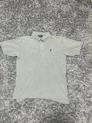 Polo Ralph Lauren piké  - Grå polo Ralph Lauren piké i jätte fint skick.  Storlek M (12/14) Hör av er om ni vill ha mått. Använd fåtal gånger. Säljer eftersom jag har vuxit ur den. Inga defekter alls. Hör av er vid frågor eller funderingar😊