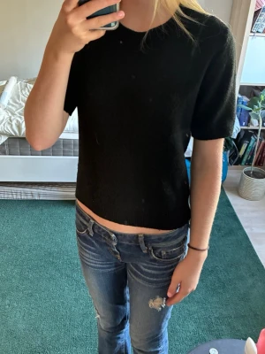 Svart stickad kortärmad topp - En enkel och stilren svart stickad topp med korta ärmar och rund hals. Modellen är något croppad och passar perfekt till jeans eller kjol. 