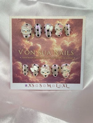 KittyDots (XS);ExtraShortAlmond  - Handgjorda press-on naglar med vit glittrig bas och rosa chrome, samt svart prickar i en glansig finish, dekorerade med Hello Kitty-motiv, vita rosetter. Extra korta mandelformade naglar. Perfekt för dig som vill ha en söt och unik look.XS: 14 mm, 11 mm, 11,5 mm, 10 mm, 8 mm