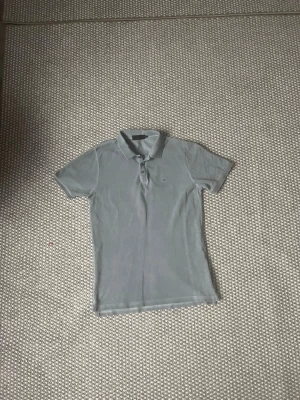  Calvin Klein  - Säljer en grå  Calvin Klein med korta ärmar och klassisk krage. Toppen har knappar framtill och är i ett mjukt material som känns skönt mot huden. Perfekt till jeans eller kjol för en clean look.