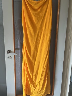 Gul långklänning med draperad front - Snygg gul långklänning med draperad front och mjukt fall. Klänningen har en enkel, ärmlös design och är tillverkad i ett lätt material som passar perfekt till varma dagar. Stilren och trendig look som sticker ut.