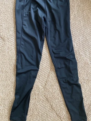 Svarta leggings i stretchigt material - Säljer ett par svarta leggings i stretchigt och mjukt material. De har en enkel design utan synliga loggor eller detaljer, och är hellånga med smal passform. Perfekta för en avslappnad och bekväm stil.