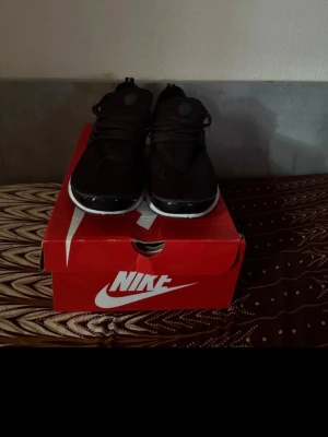 Svarta Nike sneakers med vit sula - Säljer ett par svarta Nike sneakers med vit sula och mesh-överdel. Skorna har lågt skaft, klassisk Nike-logga på sidan och elastiska snören för en sportig look. Perfekta för dig som gillar streetwear och vill ha bekväma skor till vardags.